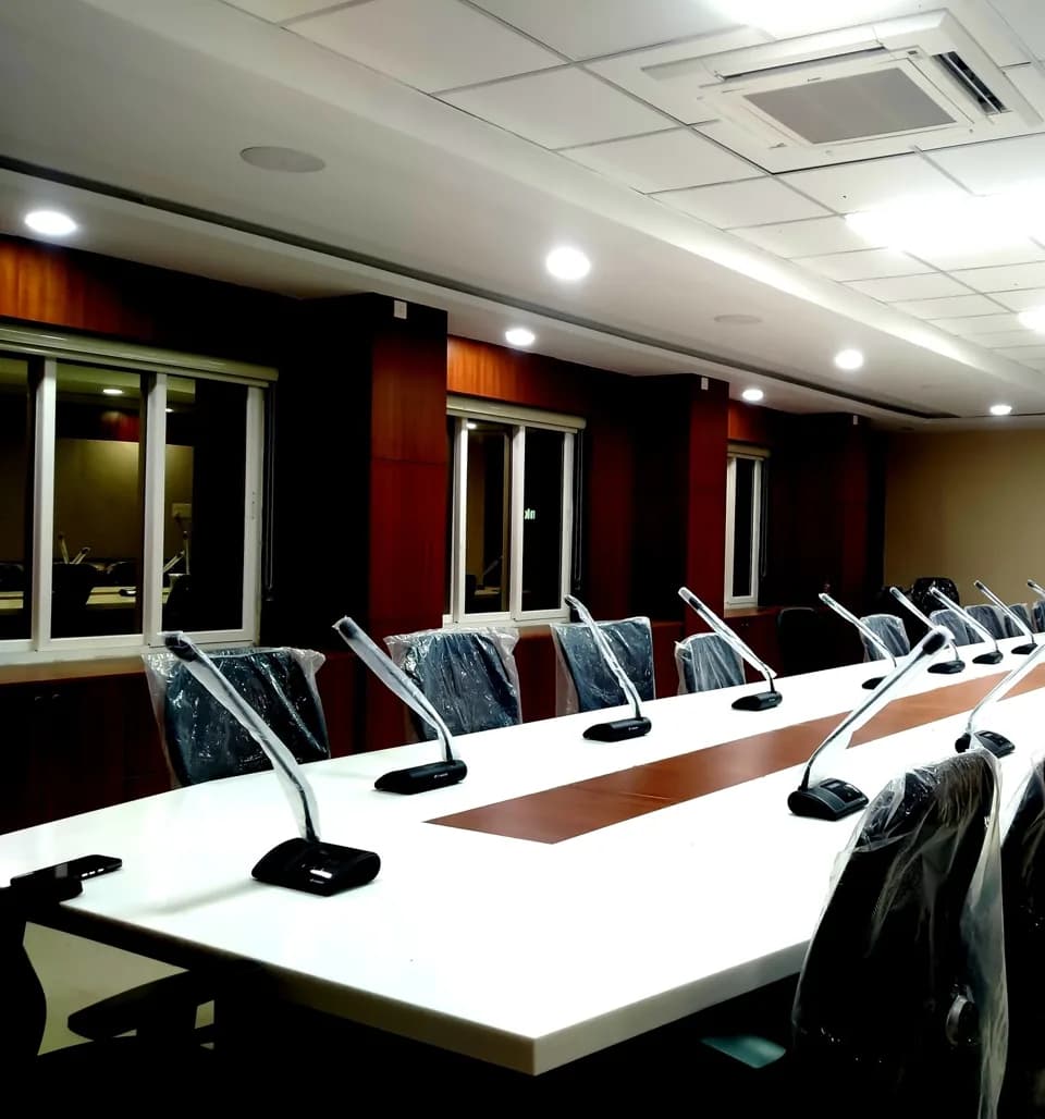 Long conference table fitted with gooseneck microphones facing a display