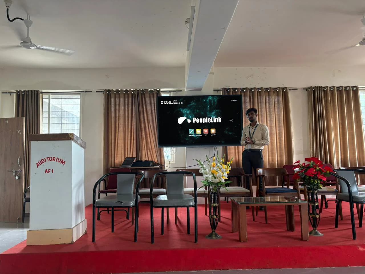 Presenter on stage beside an interactive display at an auditorium event