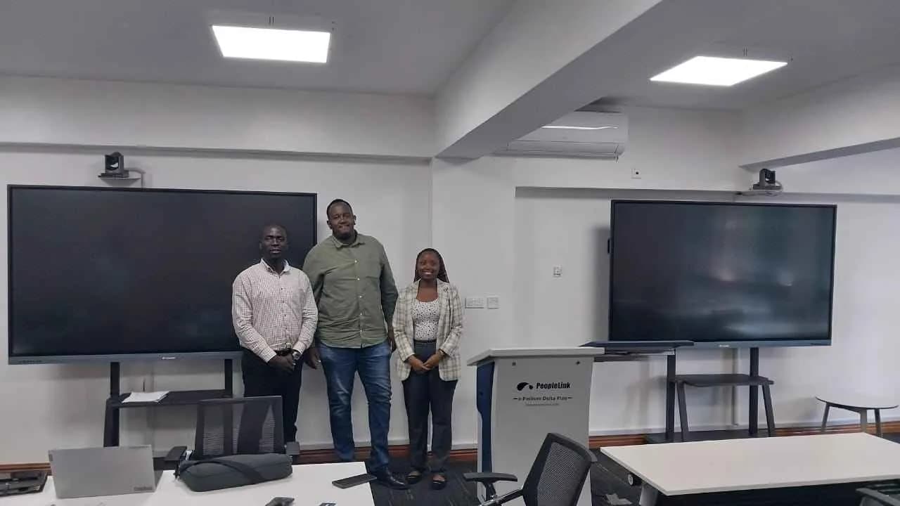 Three staff members beside two interactive displays and a digital podium in a classroom