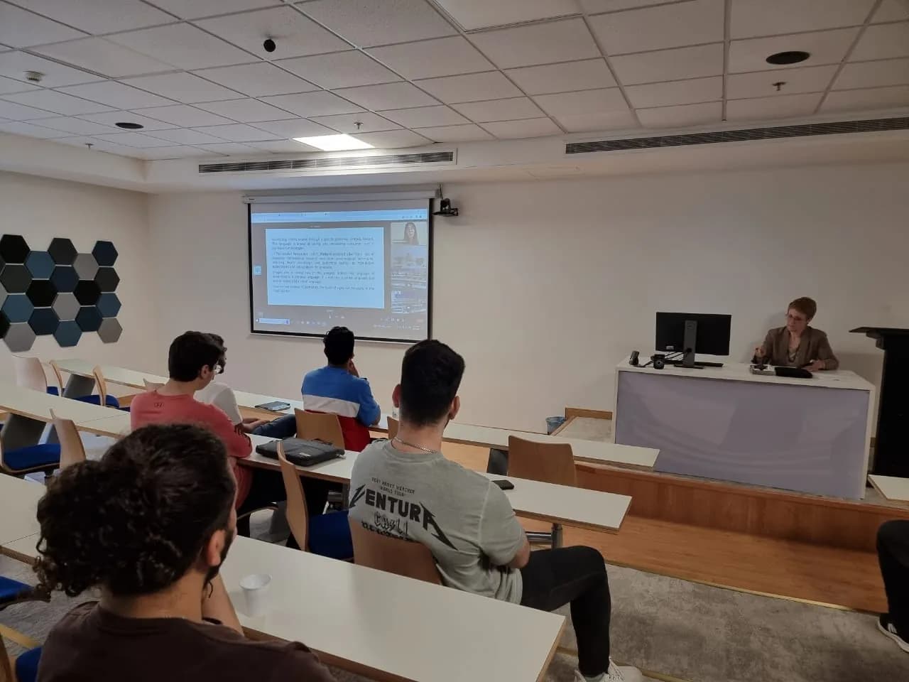 Lecture in progress with students facing a projection screen and camera